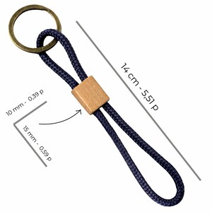 May include: A navy blue keychain with a wooden square accent and a brass ring. The keychain is 5.51 inches long and 0.39 inches wide. The wooden accent is 0.59 inches wide.