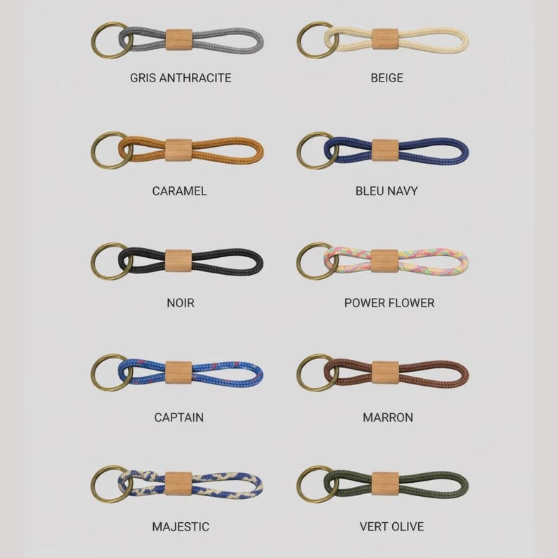 May include: A collection of keychains in various colors, each featuring a loop of rope connected to a wooden accent and a brass-colored ring. Colors include gray, beige, caramel, navy, black, and floral patterns. Text labels identify each color.