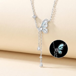 May include: A silver butterfly pendant necklace with a delicate chain. The butterfly has white and light blue wings, accented with clear crystals. The necklace features a dangling design with three teardrop-shaped crystals.