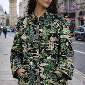 Könnte beinhalten: Eine gesteppte Jacke mit schwarzem Grund und einem sich wiederholenden Muster aus grünem Blattwerk und beigefarbenen Wildtieren. Die Jacke hat einen Stehkragen, eine Knopfleiste vorne, lange Ärmel und zwei große aufgesetzte Taschen.