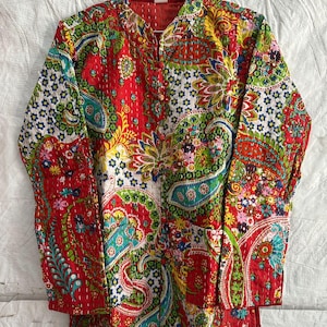 Könnte beinhalten: Eine langärmelige Jacke mit einer leuchtend roten Basis und einem mehrfarbigen Paisley- und Blumenmuster. Das Kleidungsstück verfügt über einen Stehkragen, eine Knopfleiste auf der Vorderseite und sichtbare weiße Steppnähte im Kantha-Stil.