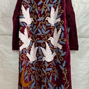 May include: A long-sleeved, deep burgundy velvet coat featuring intricate embroidery of five white doves in flight. The design includes swirling golden-brown vines, light blue leaves, and a prominent golden crescent moon at the lower left side.