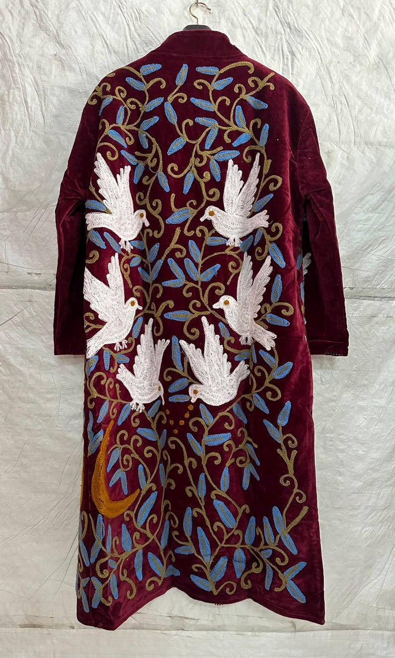 May include: A long-sleeved, deep burgundy velvet coat featuring intricate embroidery of five white doves in flight. The design includes swirling golden-brown vines, light blue leaves, and a prominent golden crescent moon at the lower left side.