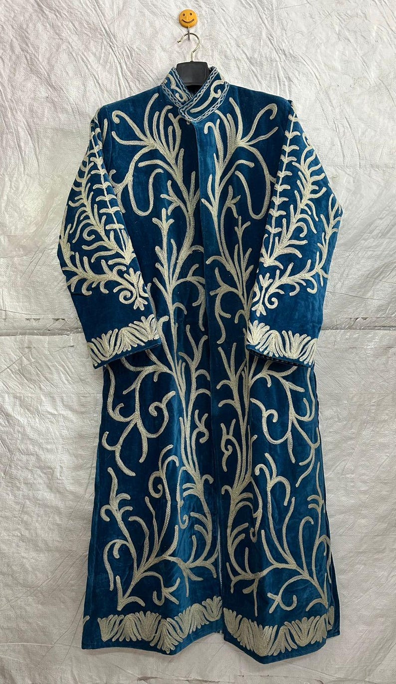 May include: A long-sleeved, knee-length coat in deep teal blue featuring intricate, light-colored embroidery in a branching, organic pattern that covers the front and sleeves. The coat has a high collar and a straight, open-front silhouette.