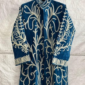 May include: A long-sleeved, deep blue velvet coat featuring an intricate, light-colored embroidered pattern of branching, vine-like motifs that extend across the front and sleeves, complete with a high collar and a structured, button-up front.