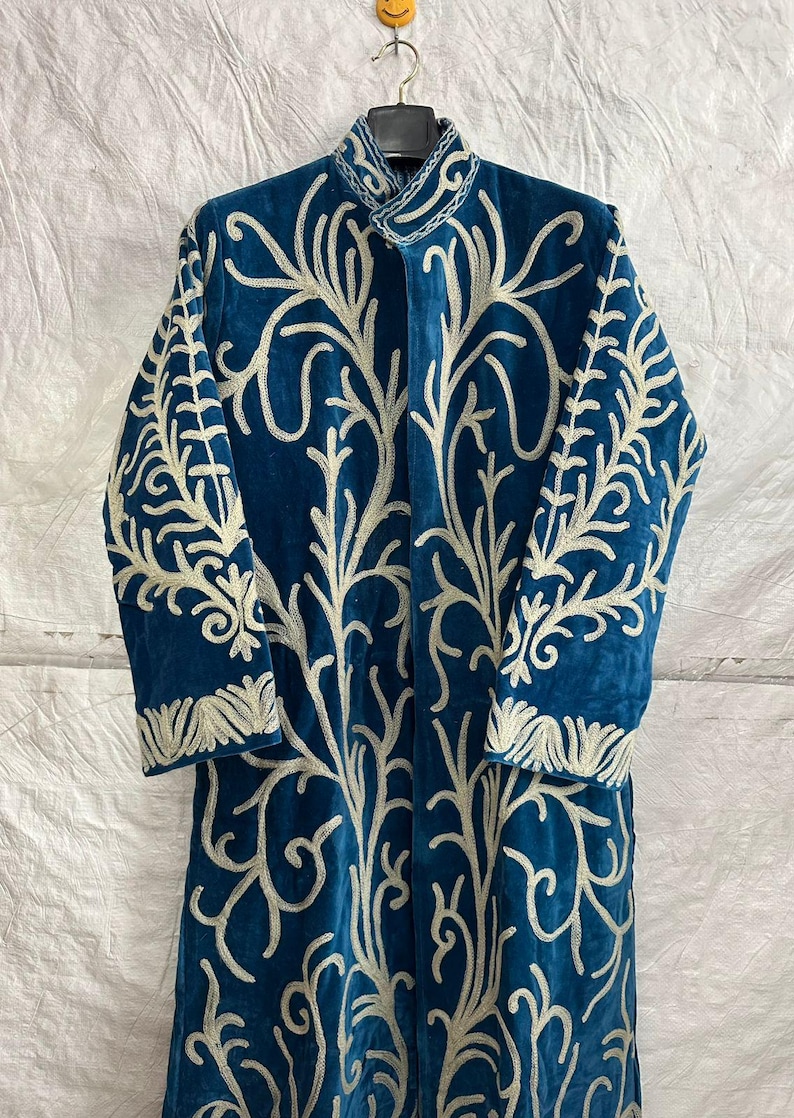 May include: A long-sleeved, deep blue velvet coat featuring an intricate, light-colored embroidered pattern of branching, vine-like motifs that extend across the front and sleeves, complete with a high collar and a structured, button-up front.