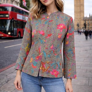 May include: A floral print jacket with a stand-up collar and long sleeves. The jacket features a button-up front and is made of a quilted fabric. The background includes a red double-decker bus and a clock tower.