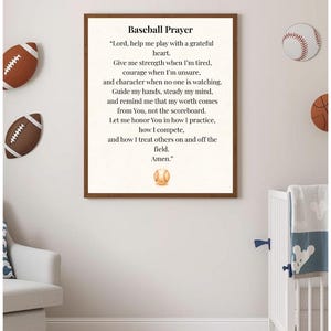 May include: A framed print with the text "Baseball Prayer" in a child's room. The prayer is printed in black font on a cream-colored background. Decorative footballs and baseballs are on the wall. A crib and armchair are also visible.