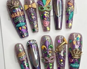 May include: A set of ten long, coffin-shaped artificial nails with a purple glitter base. Each nail features Mardi Gras-themed embellishments, including crowns, masks, musical instruments, and the text "Mardi Gras Festival" and "Parade".