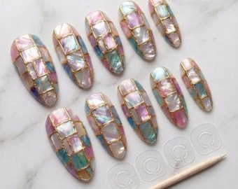 May include: A set of ten artificial nails with a mosaic design. Each nail features a grid pattern of iridescent squares in shades of pink, blue, and green, outlined with gold. Includes adhesive tabs and a wooden cuticle pusher.