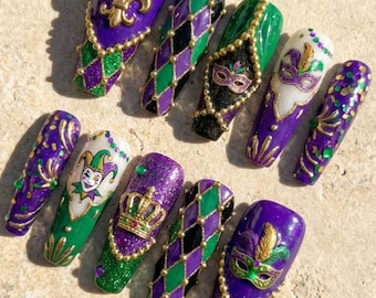 Può includere: Un set di dieci unghie finte lunghe a forma di mandorla. Le unghie presentano un tema del Mardi Gras con disegni viola, verdi e oro. Alcune unghie hanno un giglio, un giullare, una corona e maschere. Sono presenti anche glitter e perline.