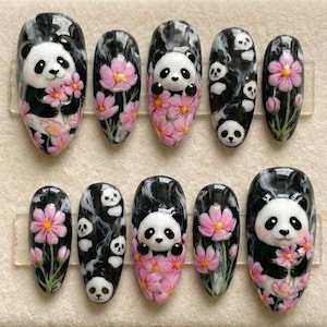 May include: A set of ten artificial nails with panda bear and floral designs. The nails feature a black and white marbled background with pink flowers and panda bear faces. The nails are oval-shaped.
