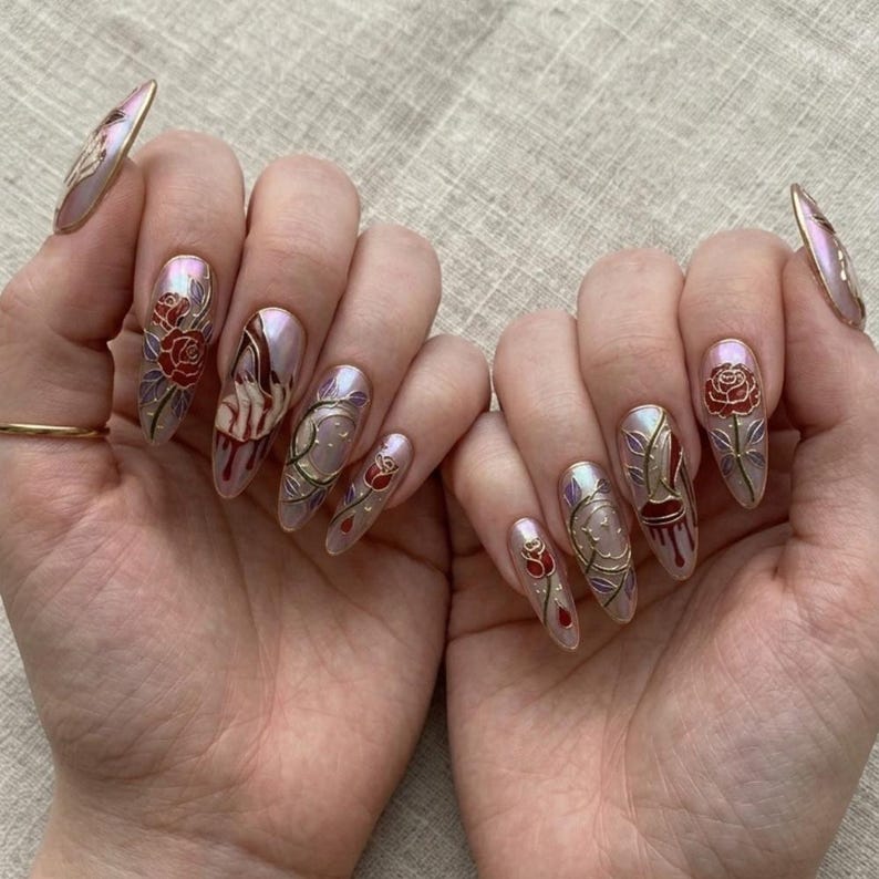 May include: Almond-shaped artificial nails with a pearlescent sheen. Each nail showcases detailed designs, including red roses, gold vines, and abstract figures. The nails are finished with a glossy top coat, set against a neutral backdrop.