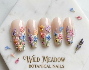 May include: Five almond-shaped artificial nails with 3D floral designs in pastel colors. Each nail features a different arrangement of sculpted flowers, including pink, blue, yellow, and purple, set against a nude base. The text "Wild Meadow BOTANICAL NAILS" is visible.