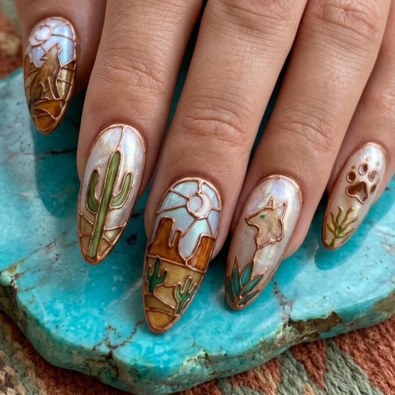 Puede incluir: Una mano con u&ntilde;as largas en forma de almendra, cada una adornada con arte &uacute;nico con tem&aacute;tica des&eacute;rtica. Los dise&ntilde;os incluyen un lobo aullando, un cactus, un paisaje des&eacute;rtico, una cabeza de coyote y una huella de pata, todo en un estilo de vidriera con contornos color cobre.