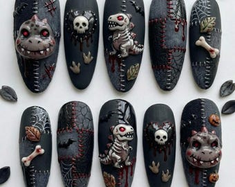 Könnte beinhalten: Ein Set aus zehn künstlichen Nägeln mit einem dunklen, strukturierten Design und 3D-Verzierungen wie Totenköpfen, Dinosaurierskeletten, Monstergesichtern, Spinnenweben, Knochen und Kürbissen, ergänzt durch genähte Muster und rote Akzente.