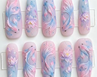 May include: A set of ten long, coffin-shaped press-on nails. Each nail features a 3D design of koi fish and lotus flowers in shades of pink, blue, and purple. The nails have a matte finish and are arranged on a clear plastic holder.