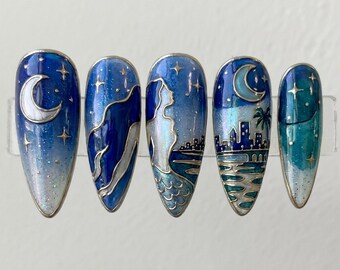 May include: A set of five almond-shaped press-on nails featuring a celestial and coastal theme. The designs include a crescent moon, a mermaid silhouette, a city skyline by the water, and starry night skies in shades of deep blue, teal, and white.