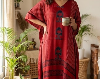 May include: A red kaftan dress featuring a V-neckline, short wide sleeves, and a dark blue printed pattern of vertical tree motifs and horizontal geometric bands. The hemline is accented with small blue tassels at the side slits.