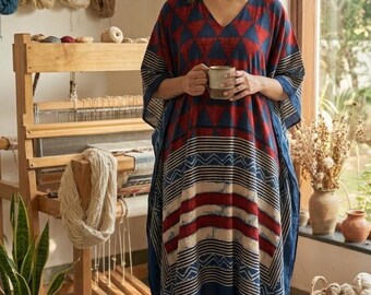 May include: A loose-fitting kaftan dress featuring a V-neckline and a vibrant pattern of red triangles on a deep blue background. The lower section displays horizontal stripes in red, blue, and cream, finished with small tassels at the hem corners.