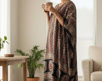 May include: A patterned kaftan dress in black, red, and beige, featuring a paisley design and tassels. The dress has a V-neck and is worn by a person holding a mug. The dress has a long, flowing design.
