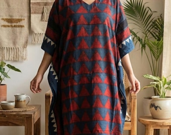 May include: A long, flowing kaftan dress with a V-neck. The dress has a repeating pattern of red triangles on a navy blue background. The sleeves and hem are trimmed with white triangles. The dress is made of a soft, flowing fabric.