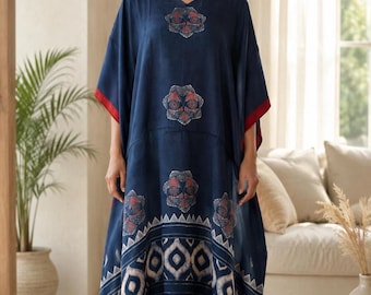 May include: A navy blue kaftan dress featuring a V-neckline, short sleeves, and a red hemline. The garment is decorated with repeating geometric floral patterns in red and white, and includes small blue tassels hanging from the bottom corners.