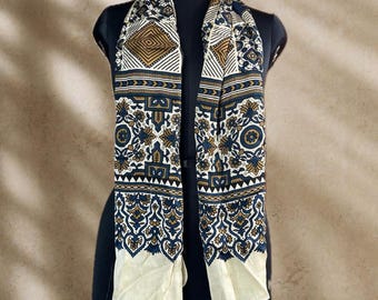 May include: A rectangular scarf featuring a cream-coloured base with a detailed print in navy blue and mustard yellow. The pattern includes geometric shapes, intricate floral motifs, and repeating border designs along the length of the fabric.