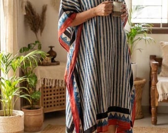 May include: A blue and white striped caftan with red trim and tassels. The caftan has a V-neck and a vertical stripe pattern. The garment is worn indoors, suggesting casual wear or loungewear. The trim features geometric designs.