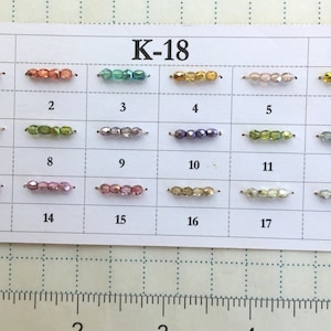 May include: A card showing multiple strands of beads in various colours, labelled with the text "K-18". Each strand has a different colour, including pink, orange, green, gold, and purple. Numbers 1 to 18 are below each strand. The beads are arranged in rows and columns.