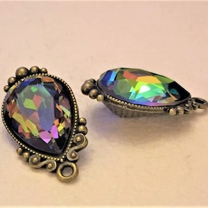 May include: Two ornate, teardrop-shaped pendants with iridescent, multi-colored crystals. The pendants have a bronze-colored metal setting with decorative detailing around the edges. One pendant is upright, and the other is on its side.