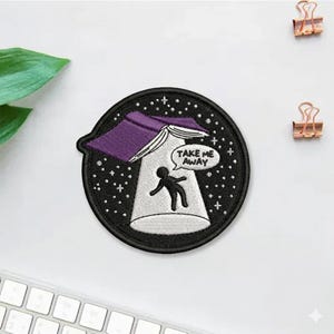 May include: Embroidered patch featuring a black and white design of a UFO beaming up a stick figure. The UFO has a purple top and the text "TAKE ME AWAY" in a speech bubble. The patch is round and has a starry background.