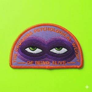 May include: Embroidered patch with a purple mask design and the text "THE CRUSHING PSYCHOLOGICAL WEIGHT OF BEING ALIVE" in orange and white. The patch features green eyes and a light purple background.