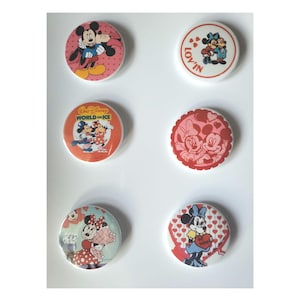 Op de afbeelding: Zes ronde Disney-personage-knoppen. Mickey Mouse en Minnie Mouse staan op de knoppen. De knoppen hebben rode, roze en witte achtergronden. Sommige knoppen hebben de woorden "LOV'IN" en "World on Ice".