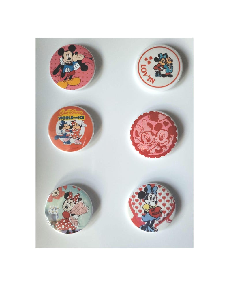 Op de afbeelding: Zes ronde Disney-personage-knoppen. Mickey Mouse en Minnie Mouse staan op de knoppen. De knoppen hebben rode, roze en witte achtergronden. Sommige knoppen hebben de woorden "LOV'IN" en "World on Ice".