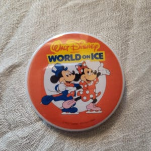 Op de afbeelding: Ronde oranje knop met Mickey en Minnie Mouse die schaatsen. De knop heeft de tekst "Walt Disney World on Ice" in wit en blauw. De personages dragen schaatskleding.