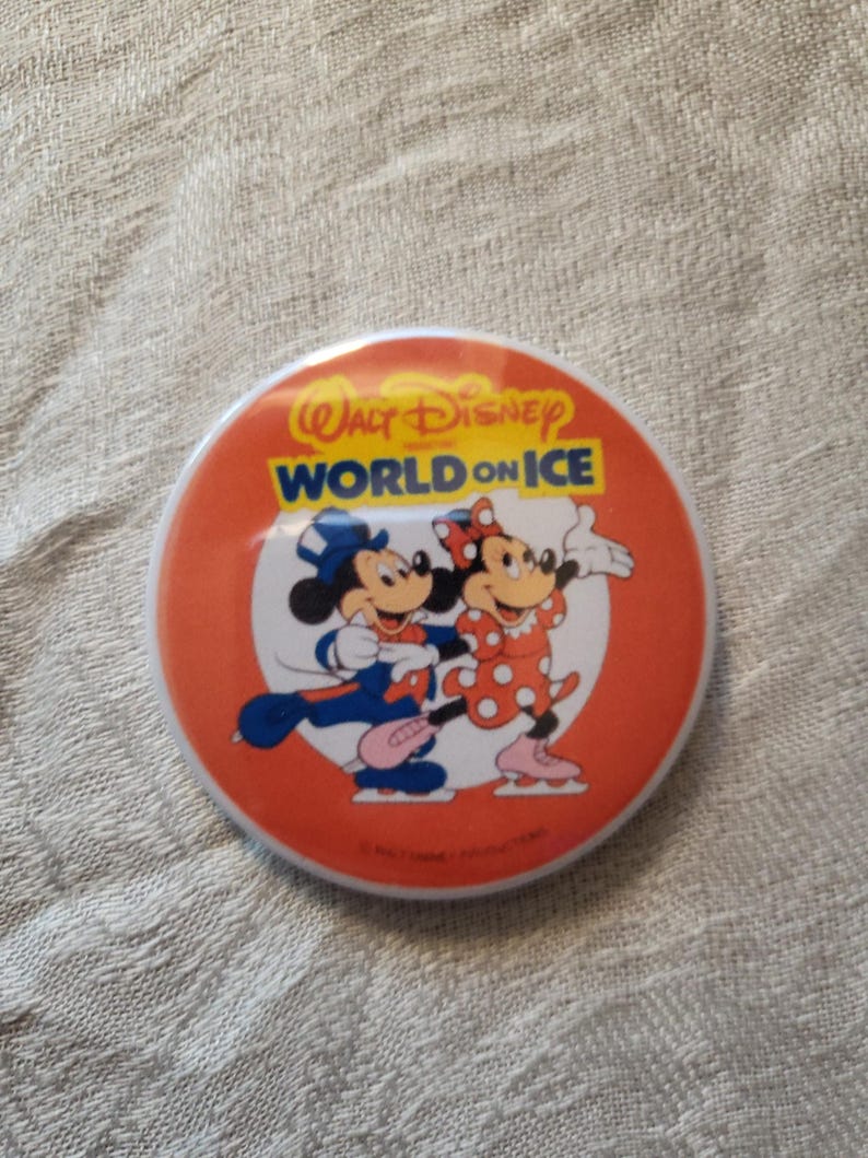 Op de afbeelding: Ronde oranje knop met Mickey en Minnie Mouse die schaatsen. De knop heeft de tekst "Walt Disney World on Ice" in wit en blauw. De personages dragen schaatskleding.