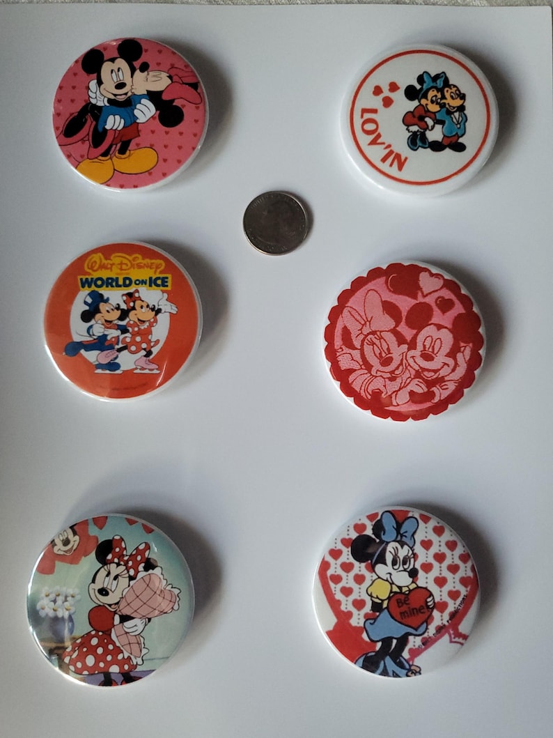 Op de afbeelding: Zes ronde Disney-personagebuttons met Mickey en Minnie Mouse. De buttons hebben Valentijnsdag- en hartthema's, met tekst als "Lov'in" en "Be mine".