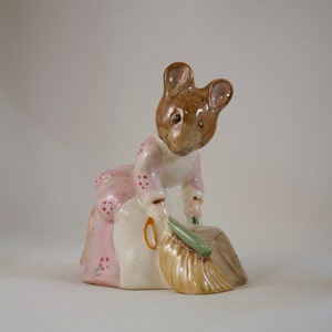 May include: A ceramic figurine of a mouse wearing a pink dress and holding a broom and dustpan. The mouse has brown fur and large ears.