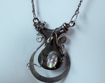 May include: A silver necklace with a unique, abstract pendant featuring a large, iridescent gemstone. The pendant is made of twisted and curved metal, creating a modern and artistic design.