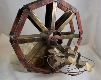 May include: A metal sculpture of a water wheel with a bird perched on top. The wheel is made of brass and has a red and brown patina. The bird is made of metal and has a silver finish.