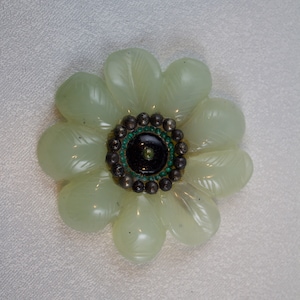 May include: A pale green jade flower brooch with a black center surrounded by a ring of green and silver beads.