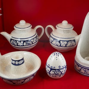 May include: Set of five ceramic pieces in a white and blue color scheme. The set includes two teapots, a candle holder, a salt and pepper shaker, and a small dish. All pieces feature a blue and white floral design.
