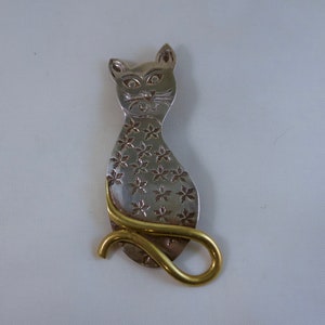 Könnte beinhalten: Eine silberne Katzenbrosche mit einem Blumenmuster und einem goldenen Schwanz.