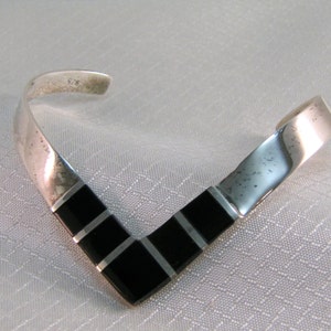 May include: A silver and black V-shaped bracelet with a black onyx inlay. The bracelet is marked "S.S."
