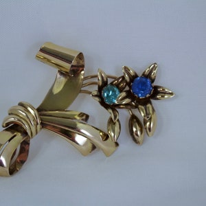 May include: Gold tone brooch with a ribbon bow and two flowers with blue and light blue rhinestones.