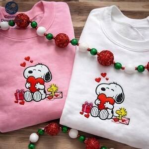 two t-shirts with a Snoopy character and a heart motif, along with a beaded necklace and red and white ornaments.