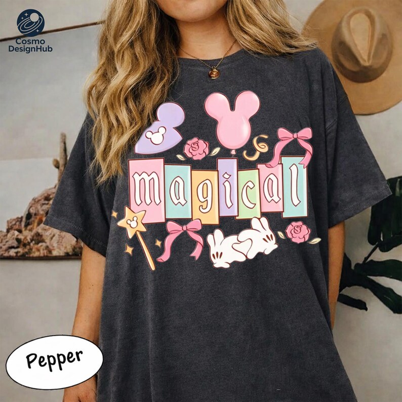 A woman wearing a black t-shirt with a colorful graphic design featuring the word "Magical" and various Disney-themed elements such as Mickey Mouse and rabbits.