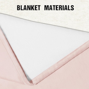 May include: A folded blanket showing two distinct layers, with the text BLANKET MATERIALS printed at the top. The top layer is a textured off-white fabric, while the bottom layer is a smooth, solid light pink fabric with stitched edges.