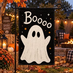 May include: A rectangular garden flag with a black background featuring a large white ghost in the center. The word "Booooo" is printed in white at the top. Small orange and white stars are scattered across the black fabric of the flag.